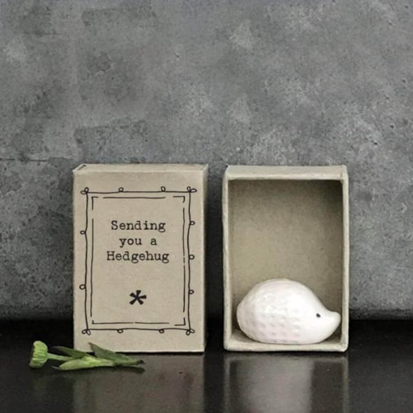 A tiny white ceramic hedgehog in a little grey cardboard matchbox printed with Sending You A Hedgehug