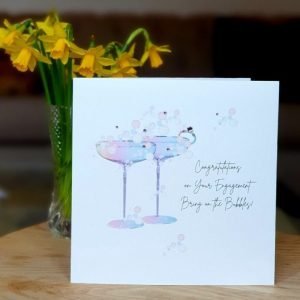 A shimmering white card with a beautiful rainbow illustration of a pair of cocktail glasses. Hand finished with genuine crystals. Congratulations on your engagement, bring on the bubbles.