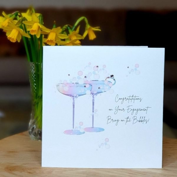 A shimmering white card with a beautiful rainbow illustration of a pair of cocktail glasses. Hand finished with genuine crystals. Congratulations on your engagement, bring on the bubbles.