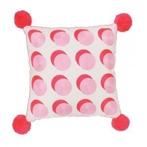 A large cream cushion with hand embroidered pink and red spots and big red pom poms at each corner