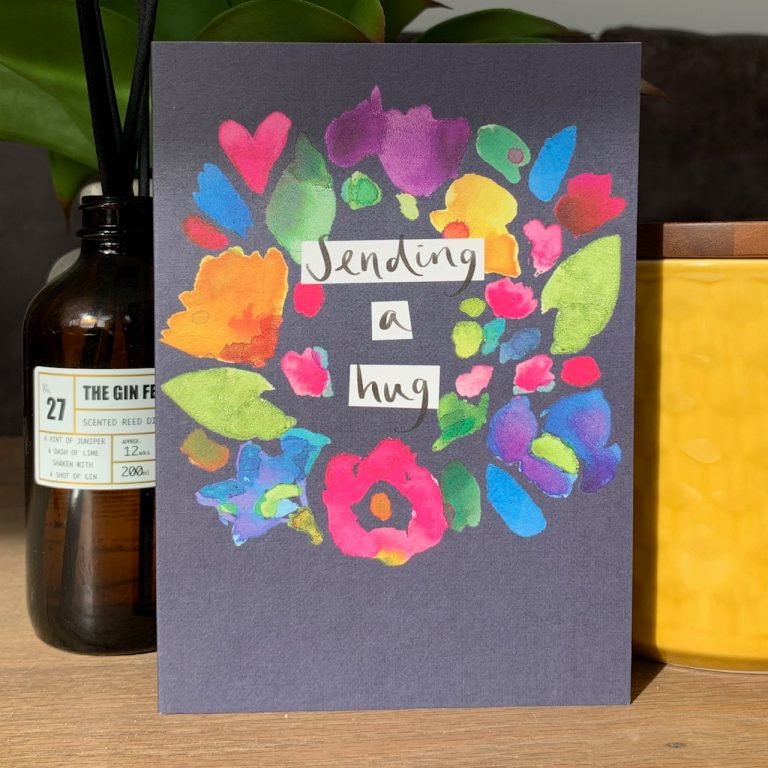 A colourful card from Sarak Kelleher with a dark blue background and colourful leaves flowers and hearts on it and the words Sending a Hug printed on it.