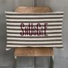 a long cushion with the word Snuggle printed in burgundy over navy and white heavy cotton ticking fabric