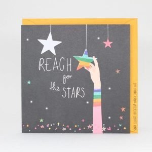 A card with a dark background and multi coloured shiny stars, spots and hearts sprinkled around. An arm reaches for a rainbow star and the words Reach for the stars