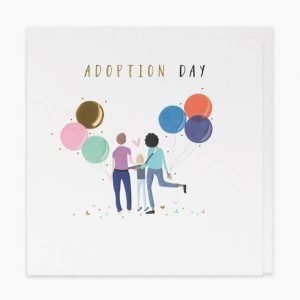 An adaoption day card with gold foil and embossed details. A couple holding 2 big bunches of balloons with their arms around a young person and the words adoption day