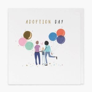 An adaoption day card with gold foil and embossed details. A couple holding 2 big bunches of balloons with their arms around a young person and the words adoption day