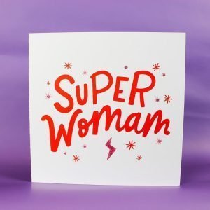A square white card with the words 'Super Womam' printed in vibrant red, with images of stars and lightening bolts around it.