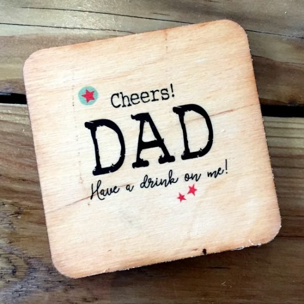A wooden coaster with the words Cheers Dad Have a drink on me printed on it.