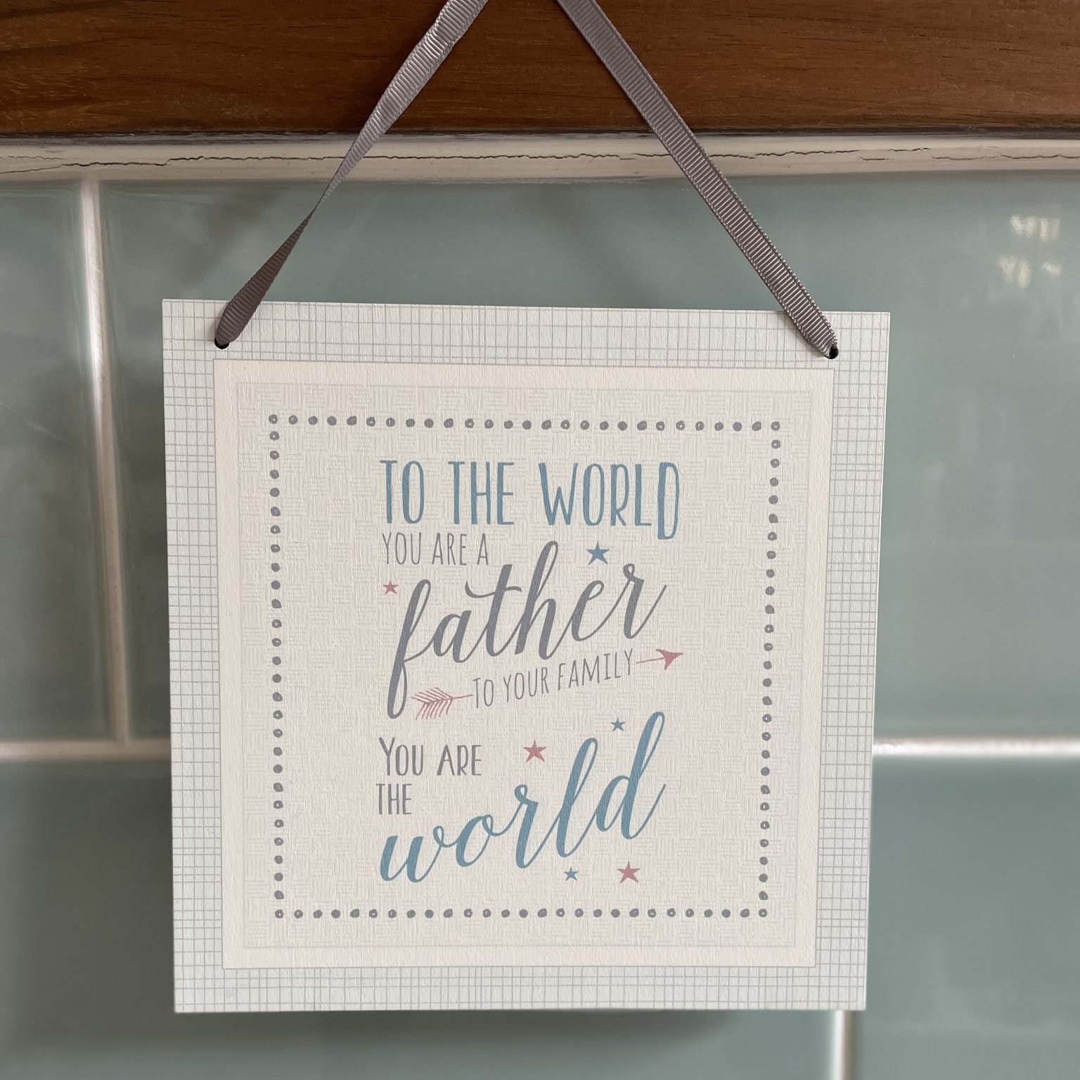 A square wooden plaque with silk ribbon hanger, with the words To the World you are a Father to your family you are the world.