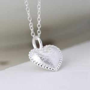 A sterling silver heart shaped pendant with an etched finish and a beaded edge on a silver chain.