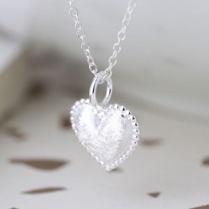 A sterling silver heart shaped pendant with an etched finish and a beaded edge on a silver chain.