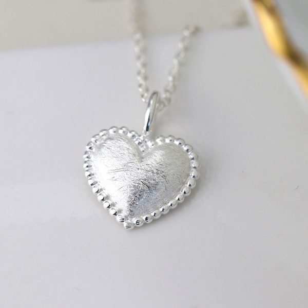 A sterling silver heart shaped pendant with an etched finish and a beaded edge on a silver chain.