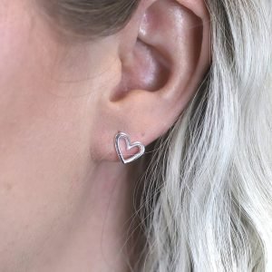 A pair of smooth asymmetric cut out heart stud earrings made from sterling silver.