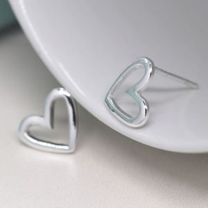 A pair of smooth asymmetric cut out heart stud earrings made from sterling silver.