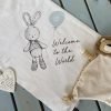 A cute blue bunny welcome muslin cloth with a design of a bunny holding a blue balloon with the words Welcome to the World on it.