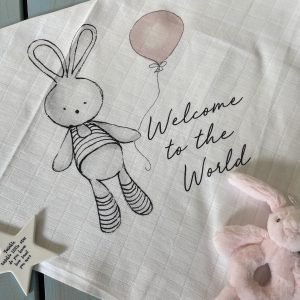A sweet square pink bunny welcome muslin to give as a gift for a new baby girl. The image is of a bunny holding a pink balloon with the words Welcome to the World printed on it.