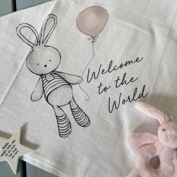 A sweet square pink bunny welcome muslin to give as a gift for a new baby girl. The image is of a bunny holding a pink balloon with the words Welcome to the World printed on it.