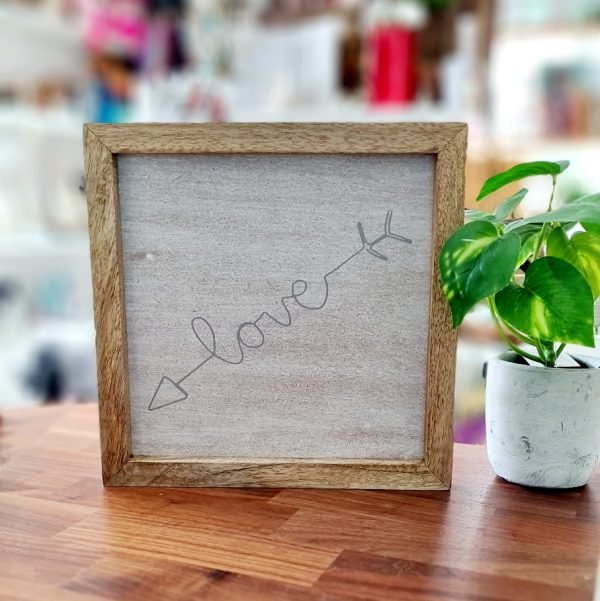 Love Arrow Wooden Panel. A panel of ash coloured wood printed with the word love in an arrow. The panel is framed in a natural wood frame