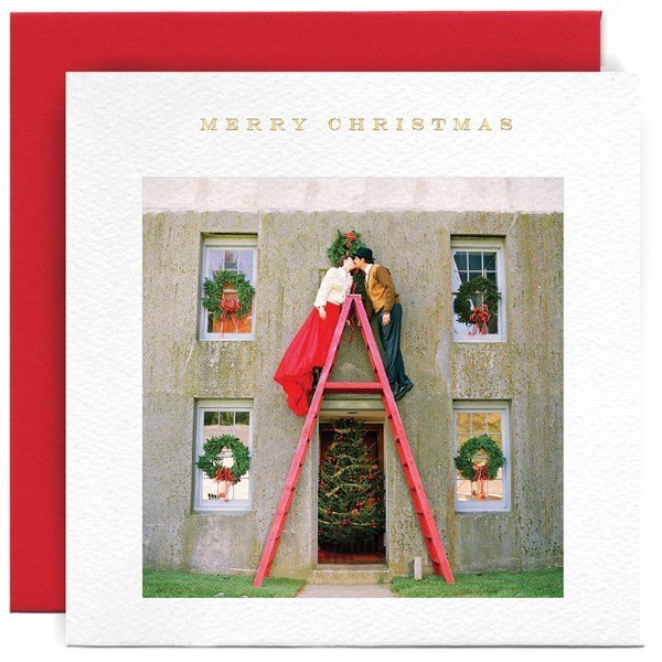 A christmas card with a photograph of a couple on either side of a step ladder decorating the outside of their house.