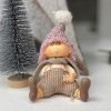 A cute sitting boy made from ceramic with beige coloured trousers. A beige scarf, Pink knitted style hat with white pompom on top.
