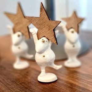 A tiny white resin santa holding a wooden star with one leg lifted