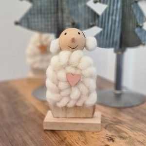 A wood and wool snow woman with a pair of ear muffs and a little pink wooden heart