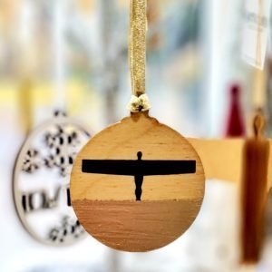 A wooden disc painted with an Angel of the North in silhouette on a gold landscape. the reverse of the disc says I believe in angels