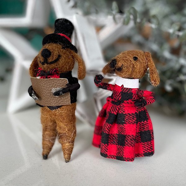 A pair of dog carol singers made from felt. One has a black top jat and a jacket and the other has a red and black checked dress