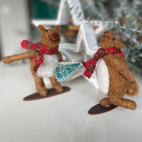 A pair of snow boarding bears made from felt. One is snowbaording with a leg in the air and the other is holding a christmas tree,
