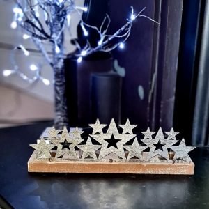 A burst of silver metalic stars of differing sizes set on a wooden plinth with 4 glass t-light holders behind the stars