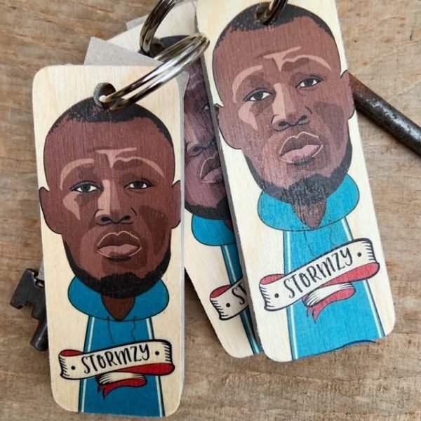 An oblong wooden block with a key ring attached and an illustration of Stormzy