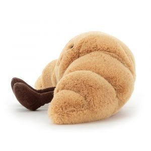 A cute cuddly toy made to look like a croissant with a cute smiley face and little chocolate coloured legs and feet.