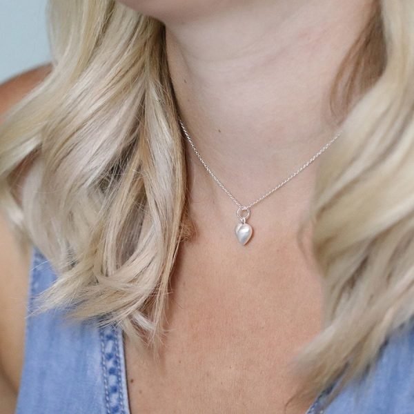 A silver chain necklace with a heart pendant in a smooth satin finish