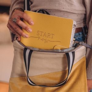 A cross body bag in velvet and gold effect faux leather. Cream and sunshine yellow velvet sections and a gold bottom and back. The bag has two handles, a hand hold and a removable shoulder strap. The handle is black and white. The bag is beautifully lined in grey sateen.