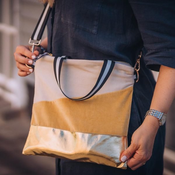 A cross body bag in velvet and gold effect faux leather. Cream and sunshine yellow velvet sections and a gold bottom and back. The bag has two handles, a hand hold and a removable shoulder strap. The handle is black and white. The bag is beautifully lined in grey sateen.