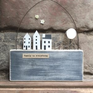 A lovely wooden scene with a blue block white wooden houses and a cute treem with a wire arch over it and the words Family is Everything printed on it.