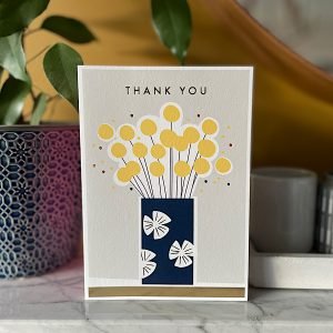 A card with a lovely vibrant bunch of flowers in a blue flower case with the words Thank You printed on it.
