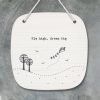 A porcelain hanging picture with an image of a couple of trees and a flying kite and the words Fly High Dream big written on it.