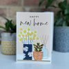 A card with an image of plants and vases of flowers and the words Happy New Home printed on it.