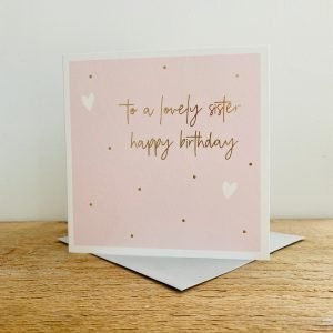 A square Pink card with gold dots and white hearts and the words To a Lovely Sister Happy Birthday in gold print