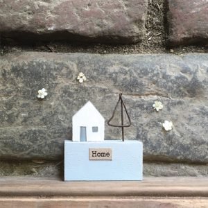 A little wooden scene with a house and a little metal tree on it and the word Home printed on it.