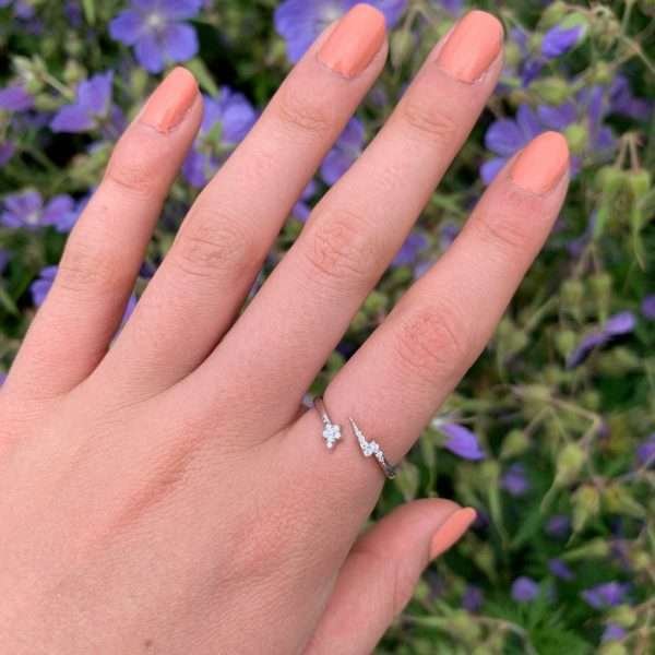 A sterling silver open ring with a pavé star at one end and a pavé lighning bold at the other