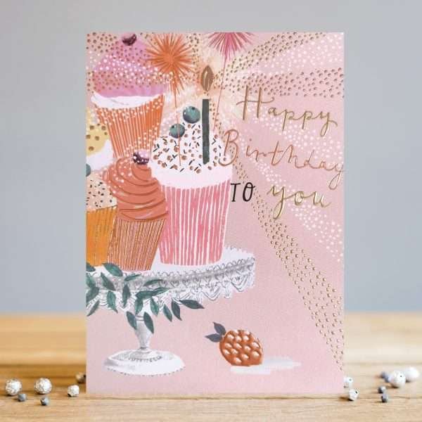 A lovely card made by Louise Tiler With a pink background and an image of a cake stand with little cupcakes on it with candles and the words Happy Birthday To You.