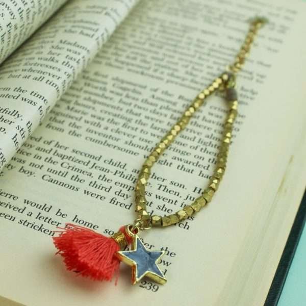 A gold bead bracelet with a slate grey enamel star pendant and a coral and gold tassel