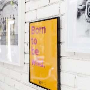 A yellow print with the words Born To Be Wild printed in a pink shimmer effect and with a QR code on the bottom of it that allows you to play the song on a Smart phone.