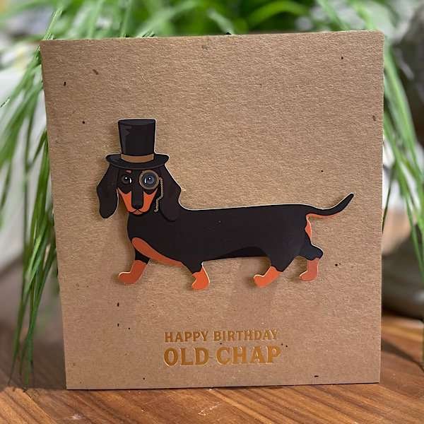 A brown kraft card with an image of a dachshund wearing a monocle and a top hat which is raised off the card giving a 3D effect.