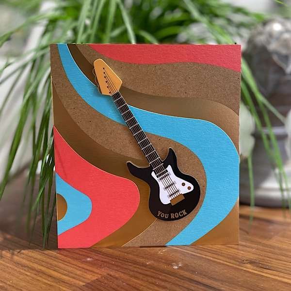 A card with colourful wavy lines all over it giving a retro style with an image of a guitar which is raised off the card giving a 3D effect.