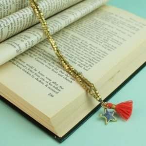 A gold bead long necklace with a slate grey enamel star pendant and a coral and gold tassel