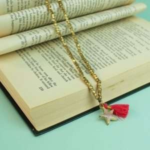 A gold bead long necklace with a nude enamel star pendant and a pink and gold tassel