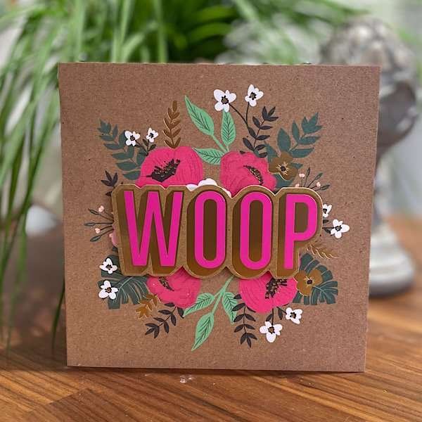 A brown kraft card with images of flowers all over it. The word woop is printed in pink and is raised off the card giving a 3d effect.
