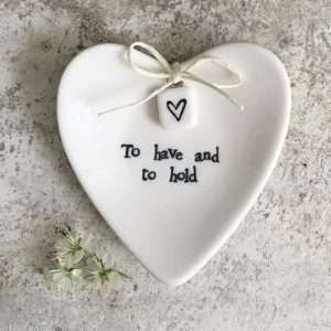 A lovely ceramic heart shaped ring dish with a little bow and square with a little heart printed on it. The dish is presented in a box with a lid. The words To Have and To Hold are written on the box as well as on the little dish.